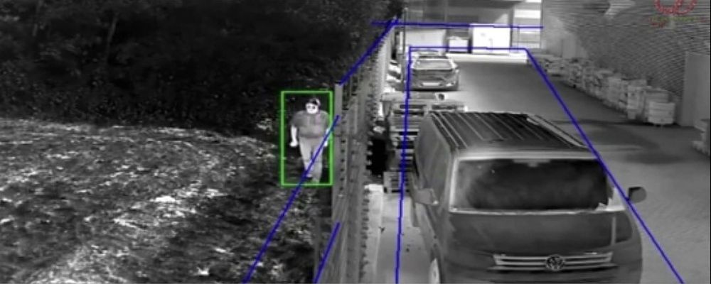 Imagen térmica de una persona caminando junto a un cerco, detectada por la analítica de intrusión