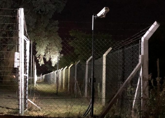 Perímetro de un country de noche con cerco eléctrico, doble alambrado y cámara sobre poste